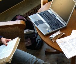 Student reading a book with a laptop computer on a table