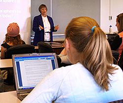 Four white female students attending a lecture by a white female professor