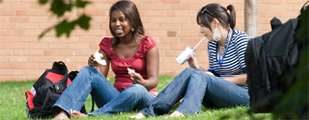 Two female students, one black and one white, enjoy lunch on the lawn of a post-secondary campus